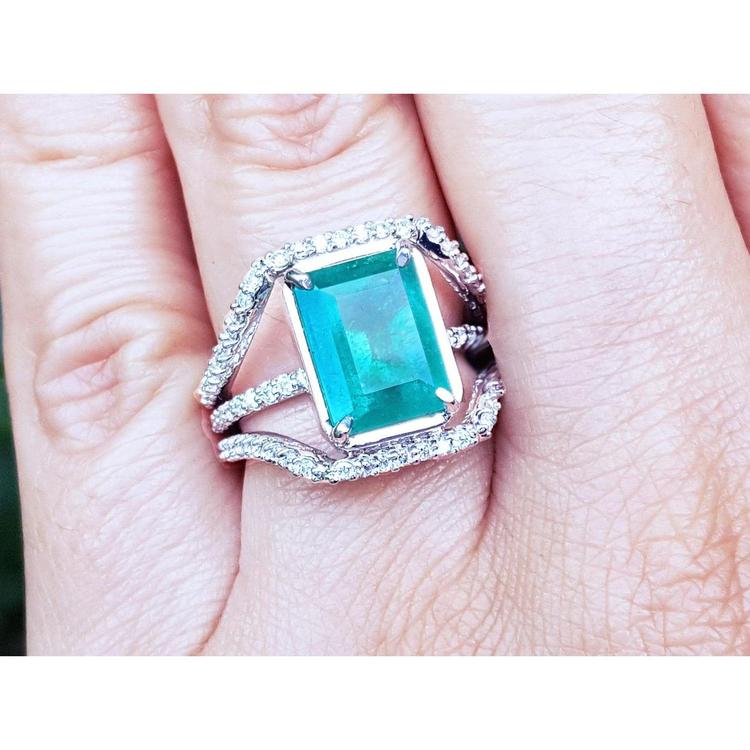 Women's emerald ring in 14k white gold with three rows of natural diamonds on a finger.
