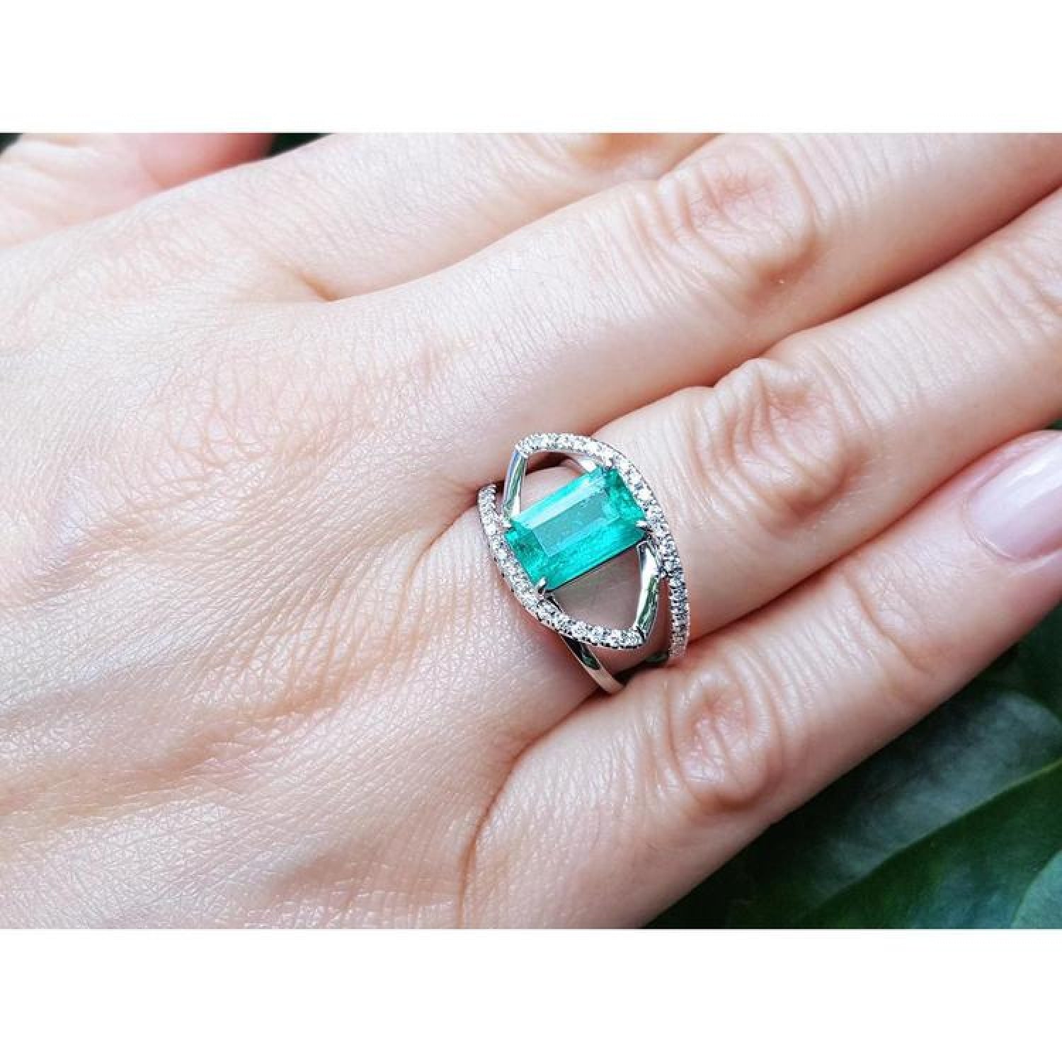 Rectangular emerald-cut emerald ring with diamond split shank in 14K white gold on a hand.