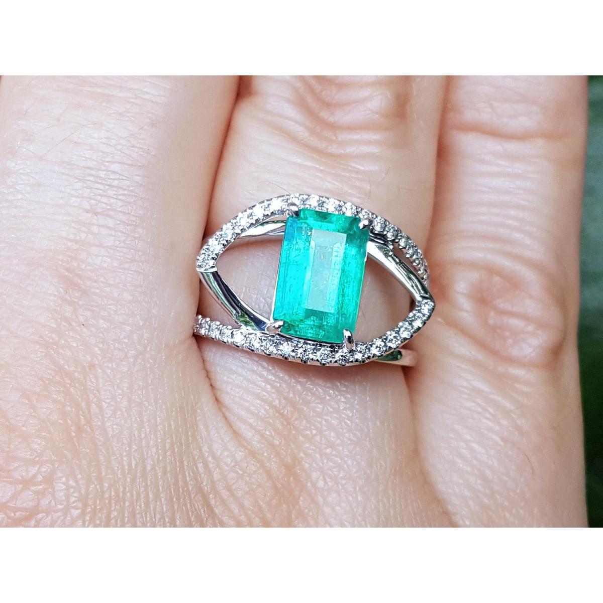 Ring with a rectangular emerald and split shank with diamonds on a finger.