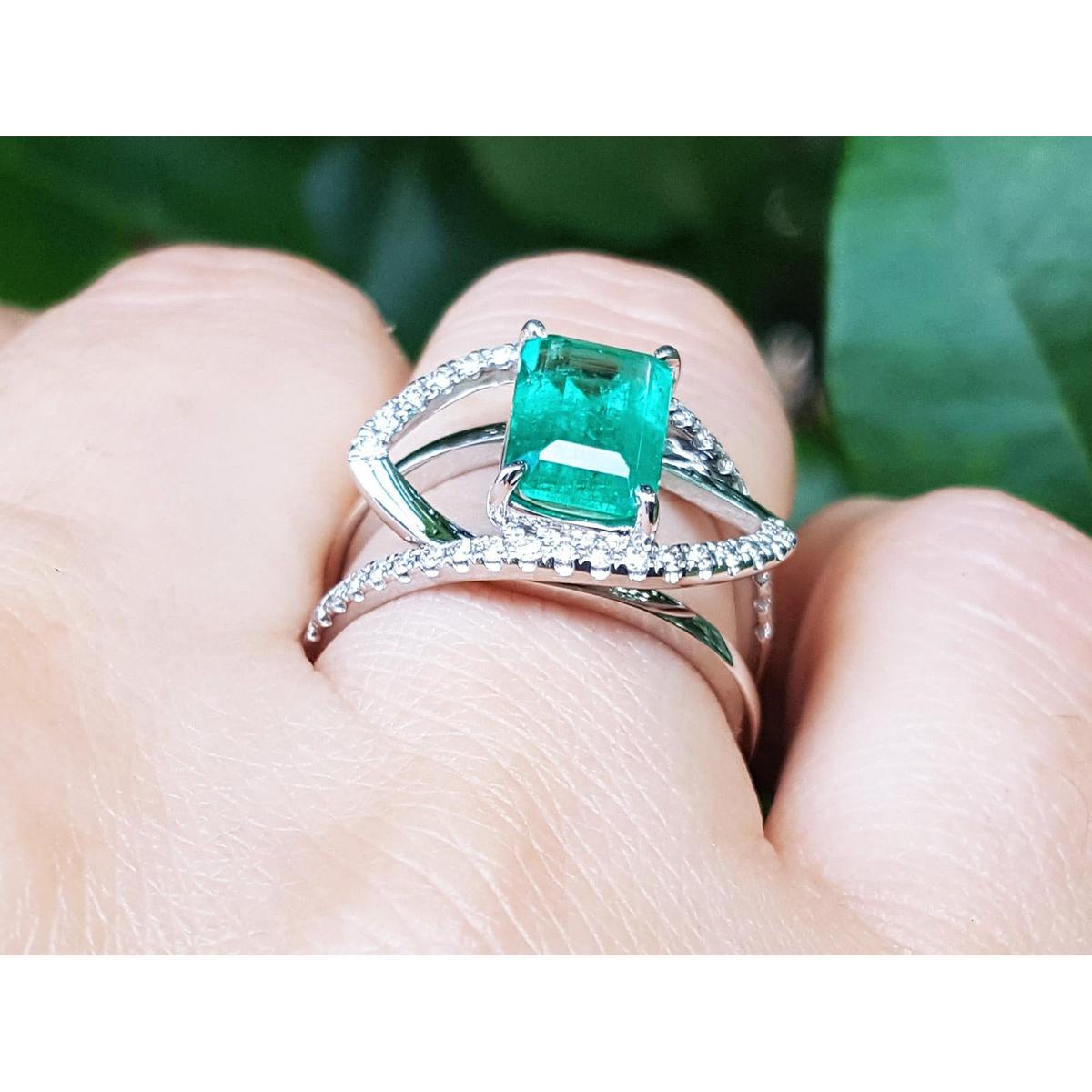 White gold ring with diamonds a top Colombian emerald on a finger against a natural background.