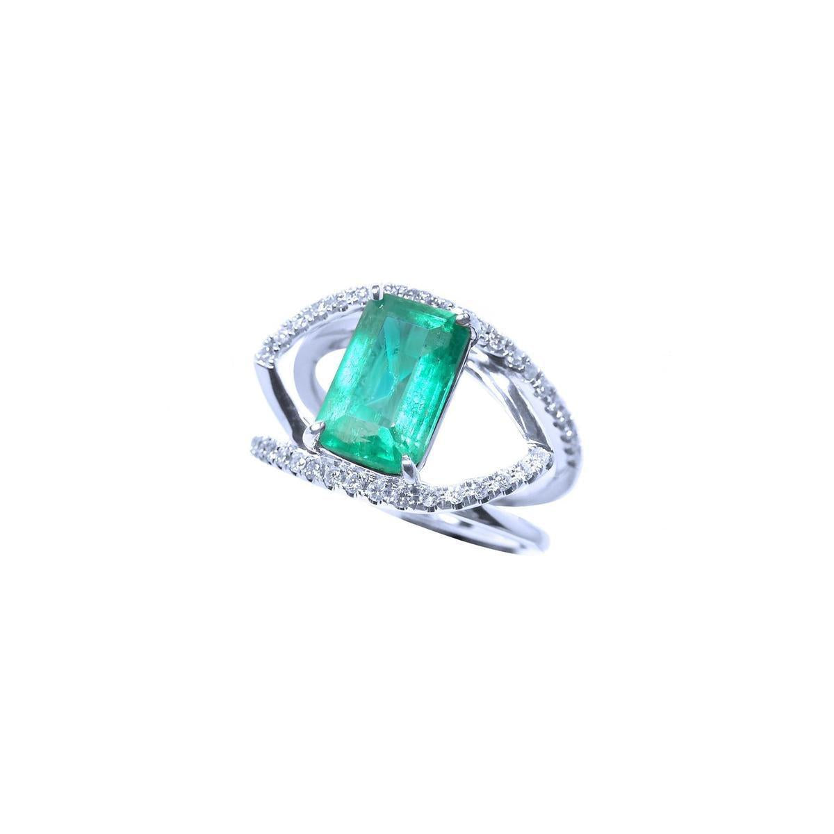 A white gold split shank ring with diamonds and a natural emerald on top.