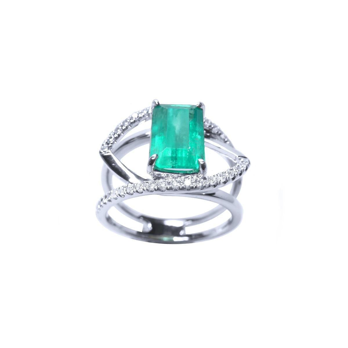 A white gold ring with a rectangular emerald on split shank with diamonds.