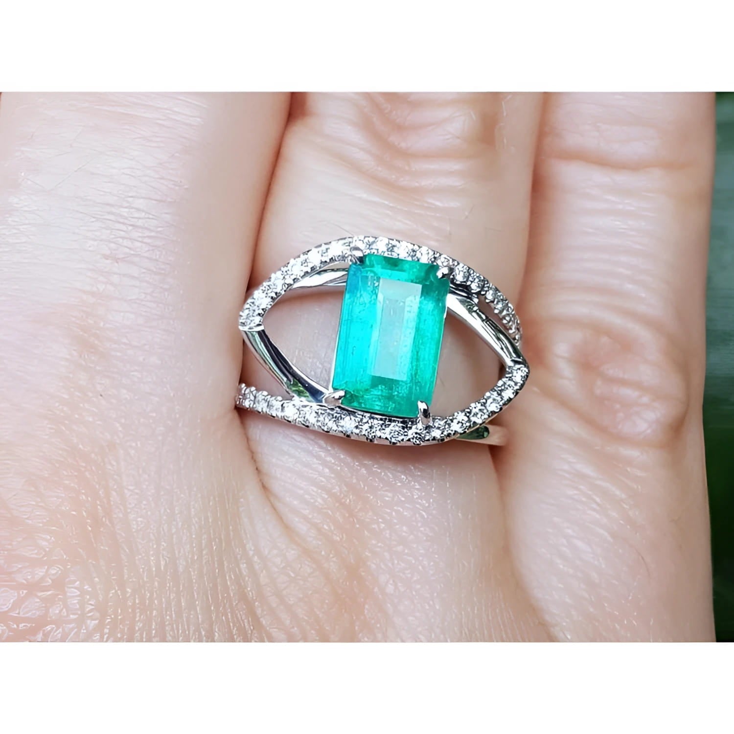 14k white gold ring with a rectangular emerald and split shank with natural diamonds on a finger.