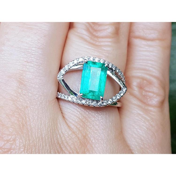 14k white gold ring with a rectangular emerald and split shank with natural diamonds on a finger.