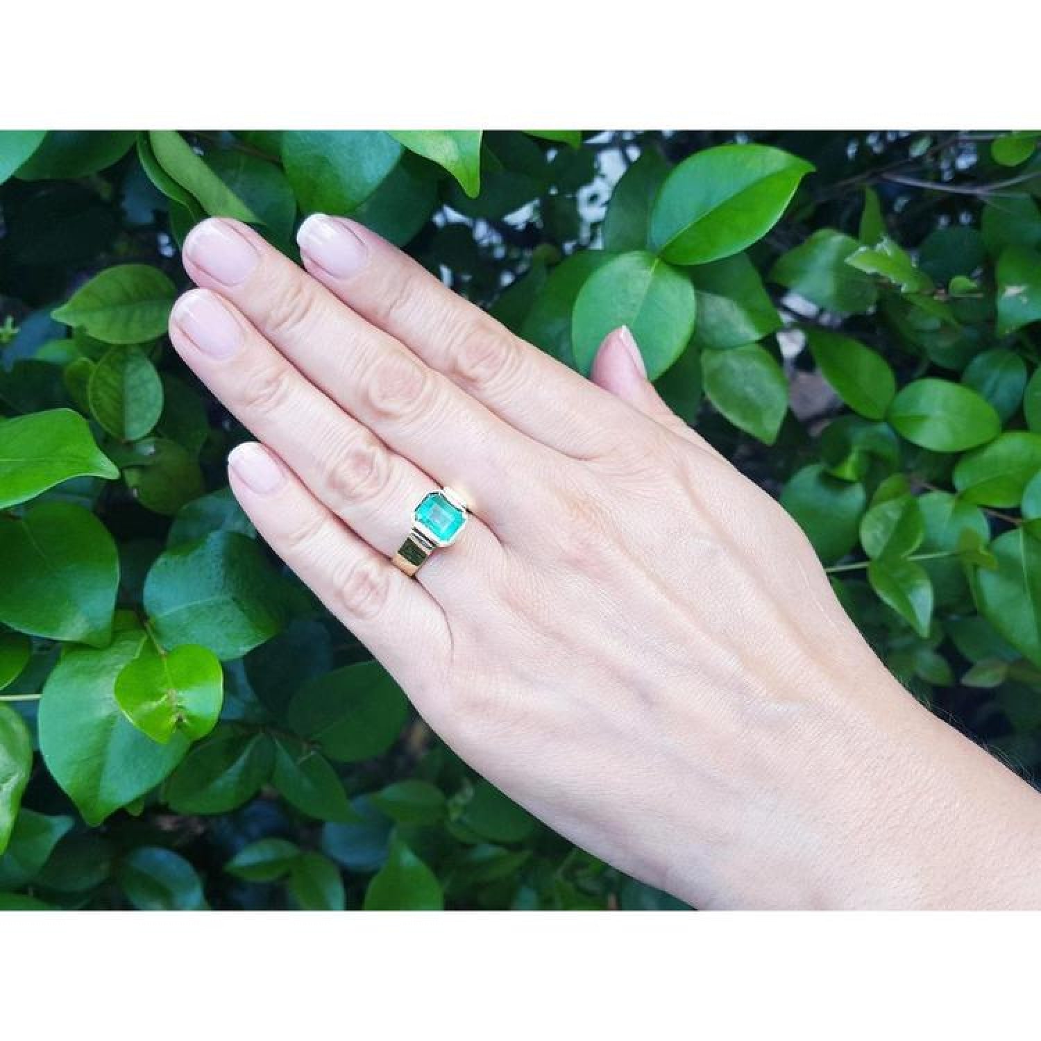 Emerald-cut emerald solitaire ring, bezel set in high-polish 14K gold, worn on a hand.
