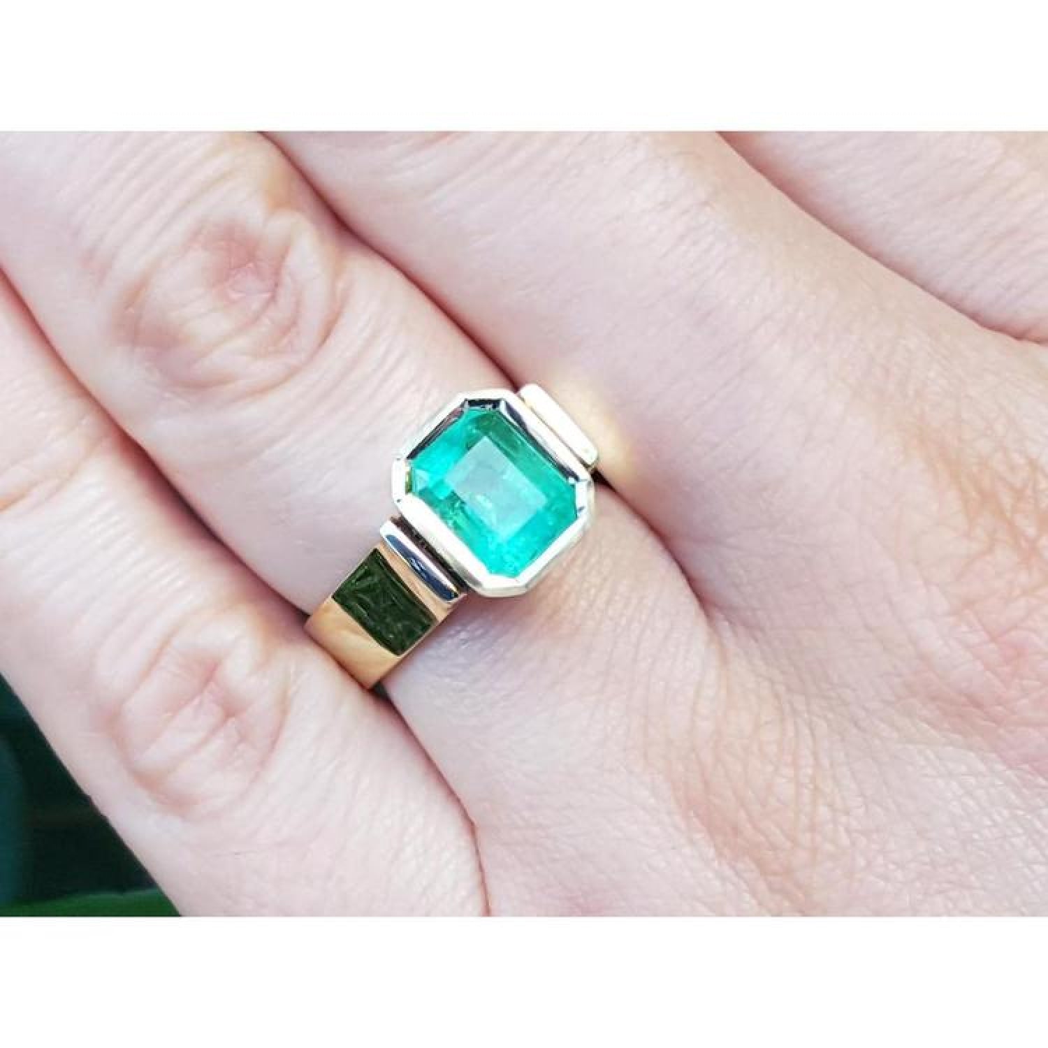 Emerald-cut 2.05 ct. emerald solitaire ring, bezel set in high polish 14K gold on a hand.