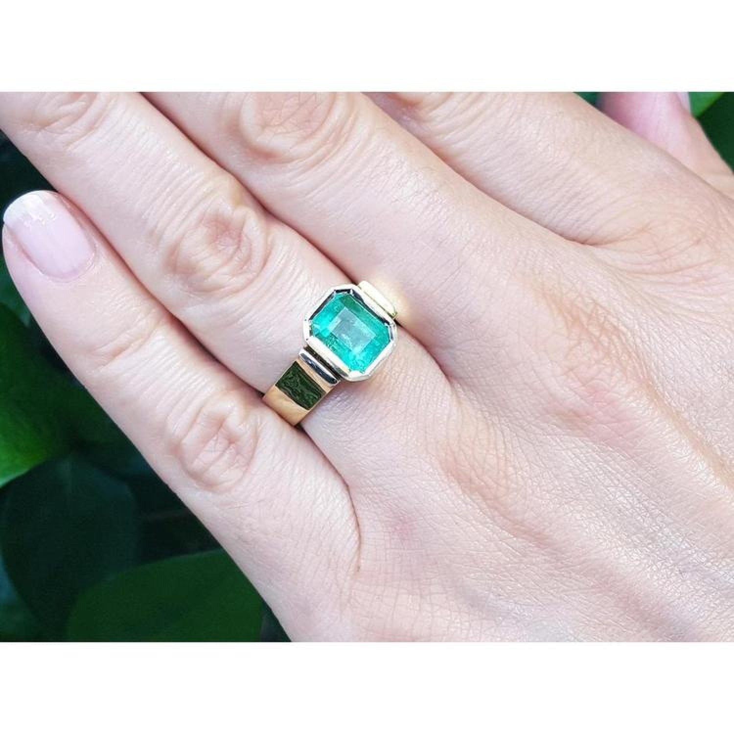 Emerald-cut emerald solitaire ring, bezel set in high polish 14K gold, worn on a hand.