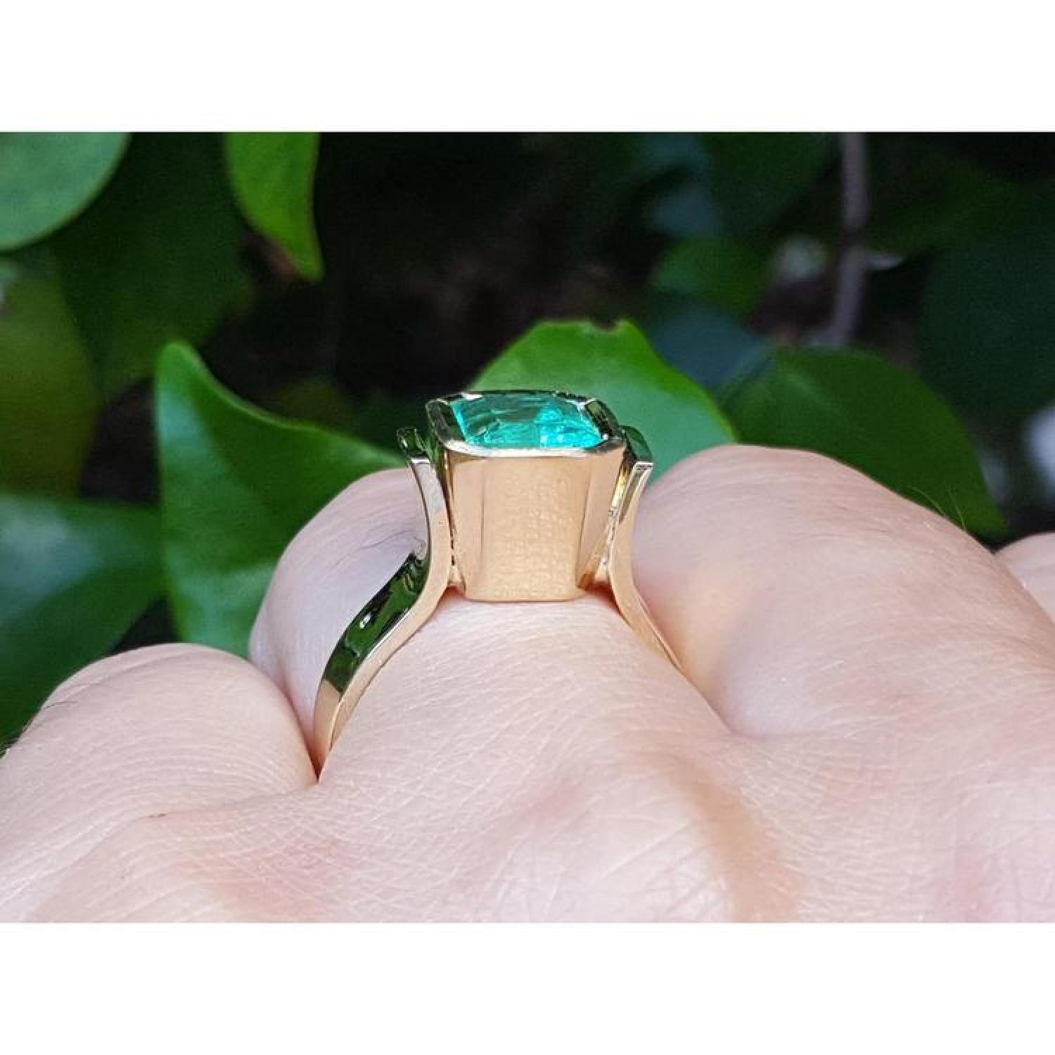 Emerald-cut emerald solitaire ring, 2.05 ct, bezel set in high polish 14K gold on a finger.