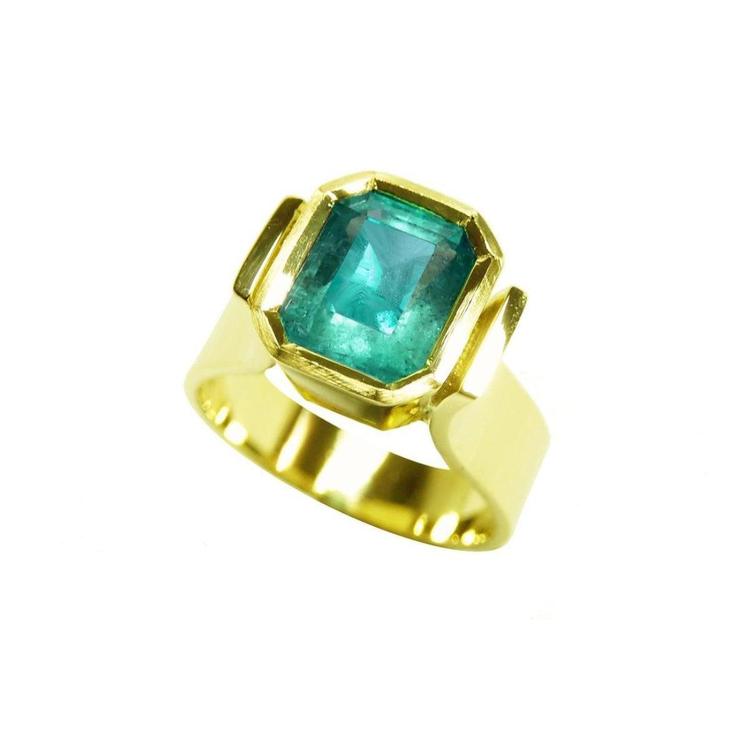 A solitaire colombian emerald ring for women in 14k yellow gold bezel set emerald-cut.