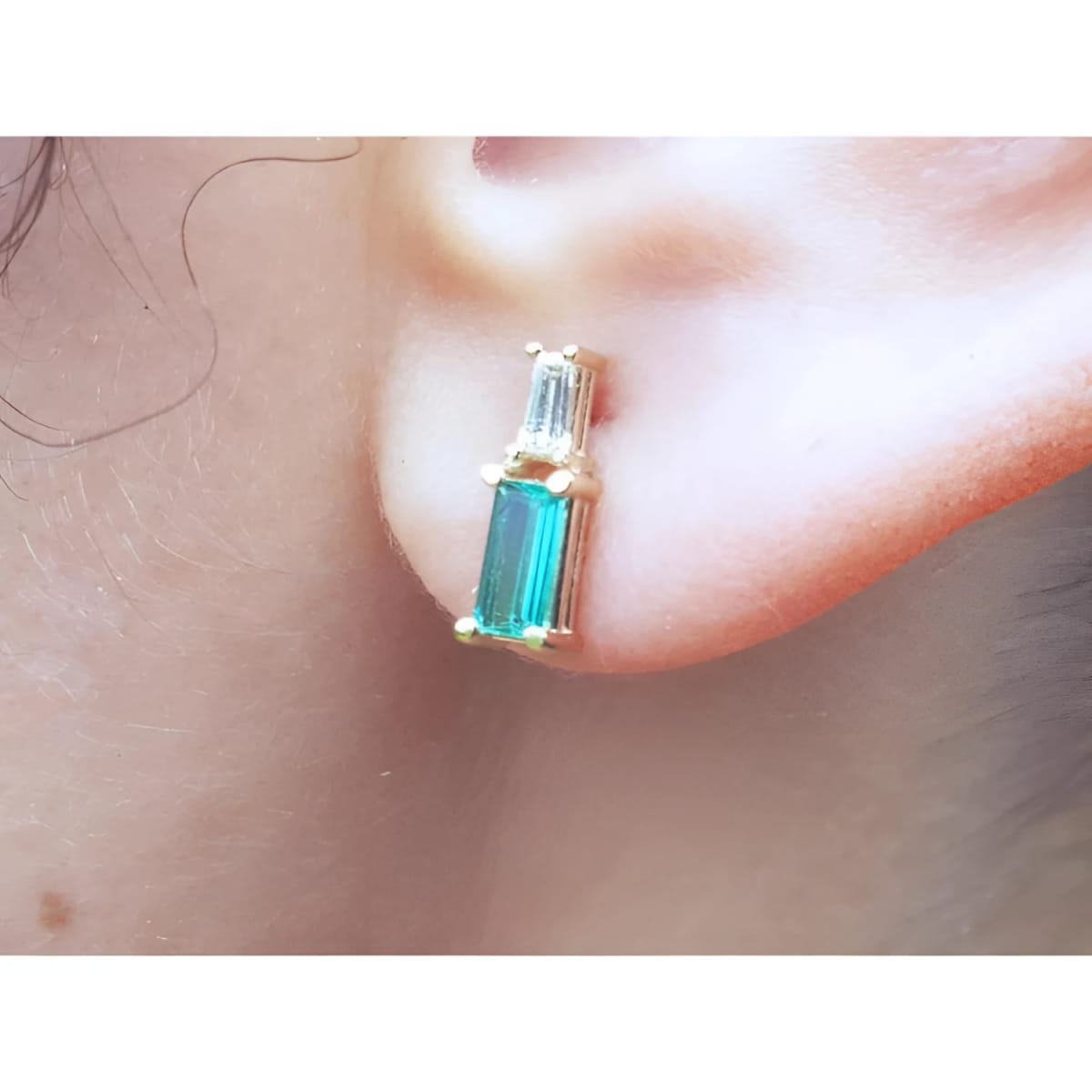 Natural baguette cut colombian emerald and diamond stud earrings worn on an ear.