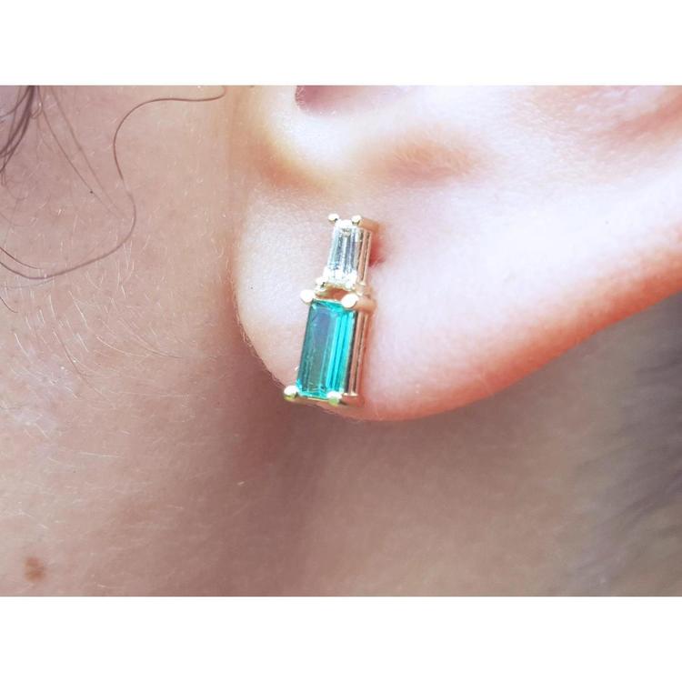 Natural baguette cut colombian emerald and diamond stud earrings worn on an ear.