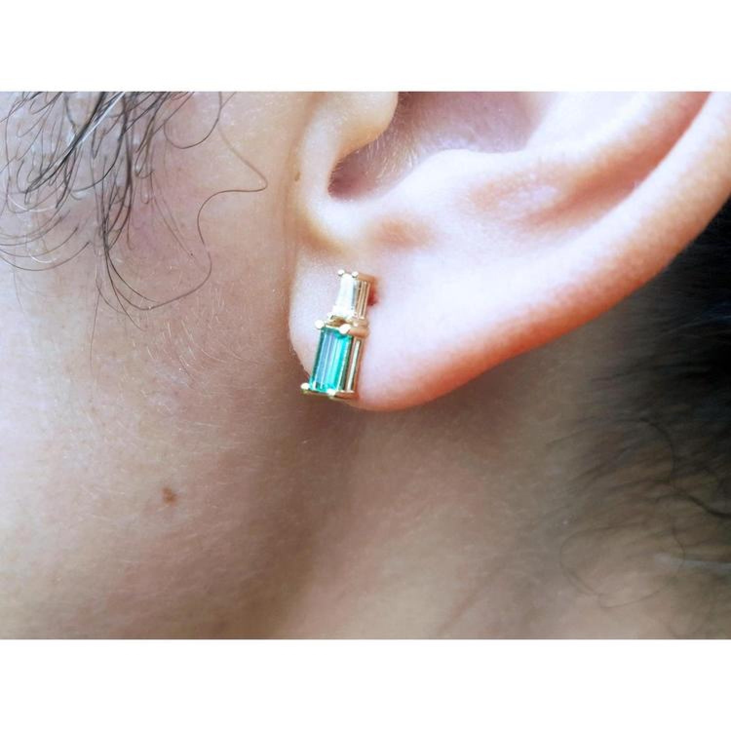 Gold baguette emerald and diamond stud earring on an ear.