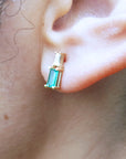 Yellow gold baguette cut emerald and diamond stud earring worn on an ear.
