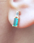 Natural baguette cut emerald and diamond stud earrings worn on an ear.