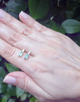 Two small emerald earrings held between fingers against a blurred green background.