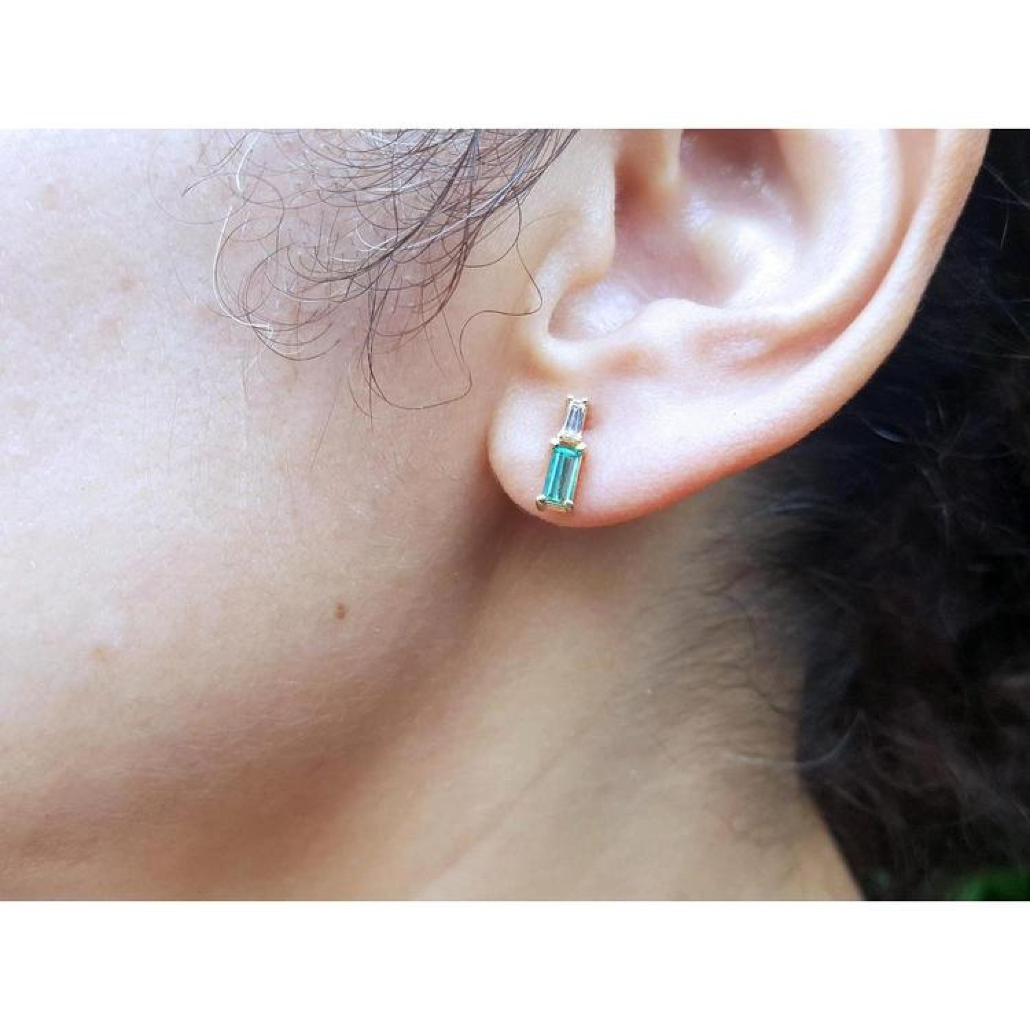Minimalist 14K gold stud earring with baguette emerald and tapered diamond accents on an ear.
