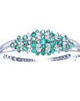 The topside profile of a white gold bangle bracelet with emeralds and diamonds on a white background.