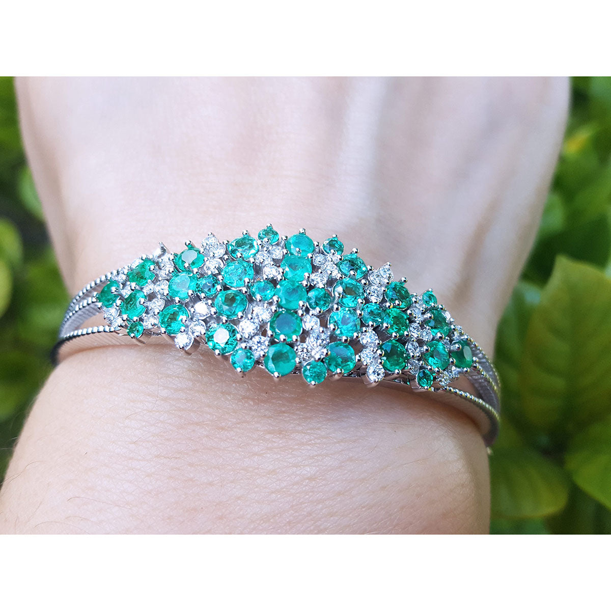 A round cut emerald bangle bracelet natural diamonds crafted in 14k white gold on a wrist.