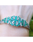 A round cut emerald bangle bracelet natural diamonds crafted in 14k white gold on a wrist.