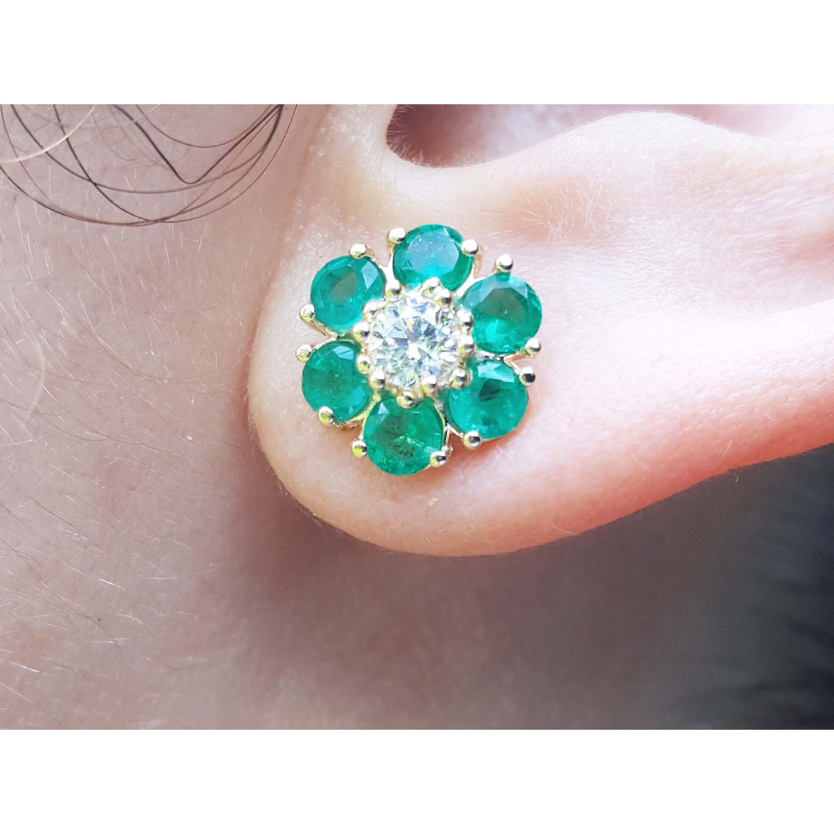 Close-up of a diamond and emerald cluster earring on an ear.