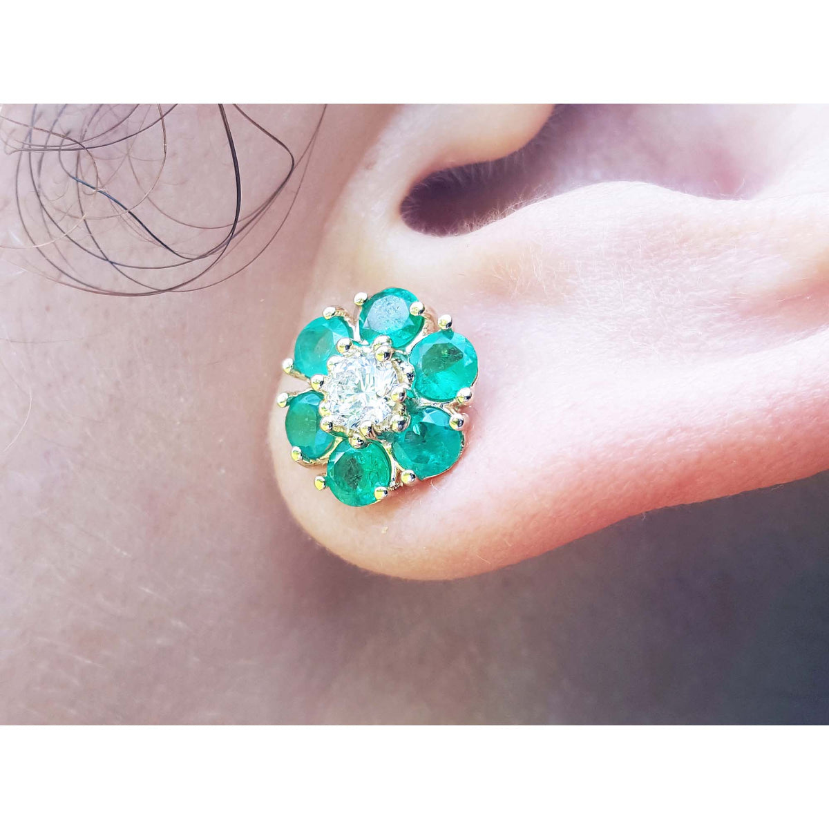 Close-up of a cluster emerald and diamond stud earring worn on an ear.