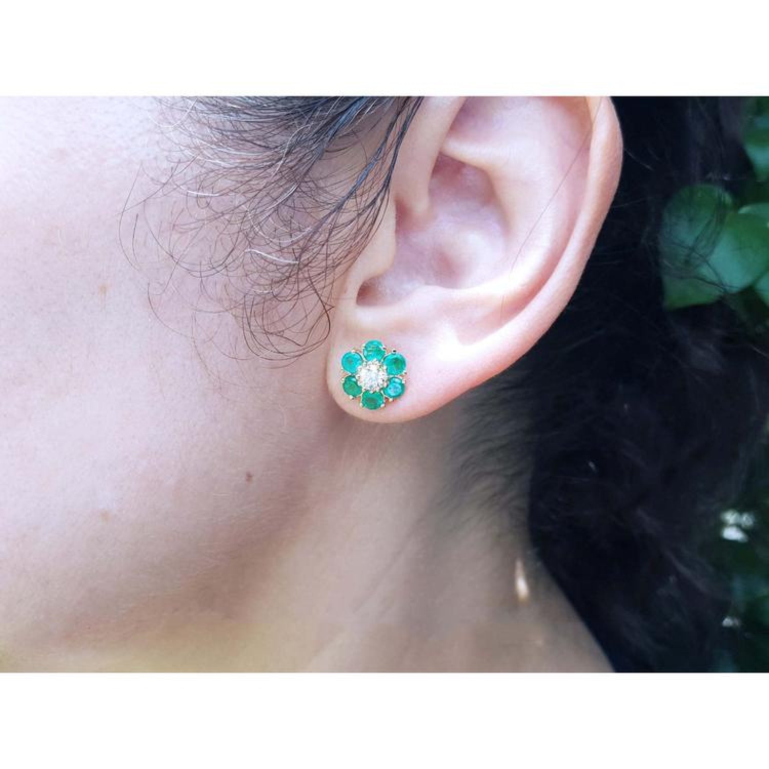 18K yellow gold flower cluster earring with Colombian emeralds and a diamond center on an ear.