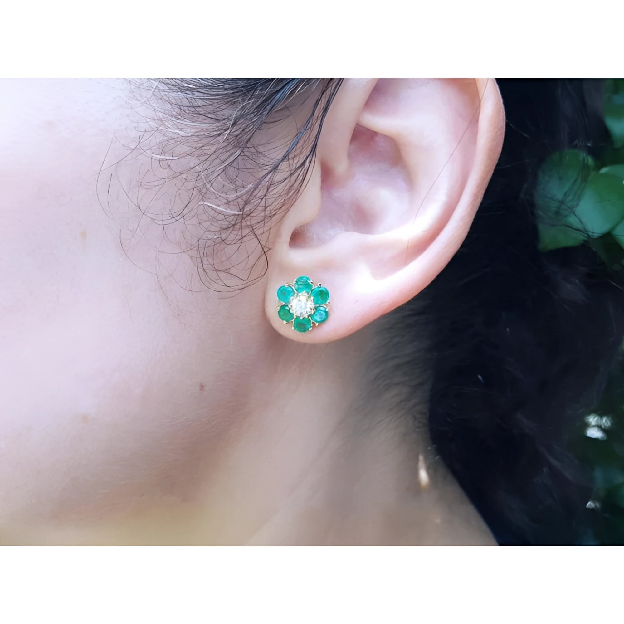 18K yellow gold flower cluster earring with Colombian emeralds and a diamond center on an ear.