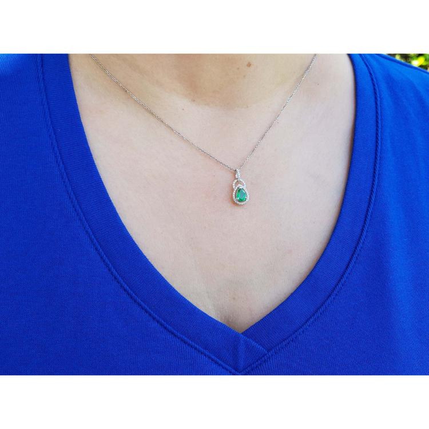Pear-shaped Colombian emerald and diamond halo pendant on a delicate 14K white gold chain, worn on a blue shirt.