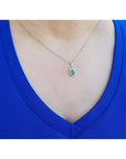 Necklace with an emerald pendant worn by a person in a blue top.