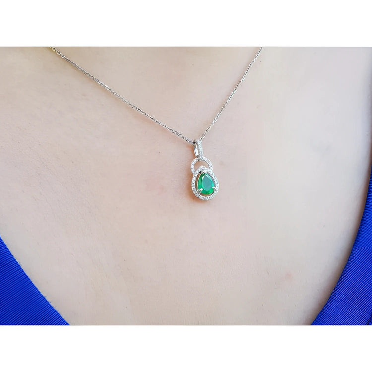 White gol necklace with a teardrop emerald pendant on a person wearing a blue top.