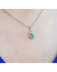 White gol necklace with a teardrop emerald pendant on a person wearing a blue top.
