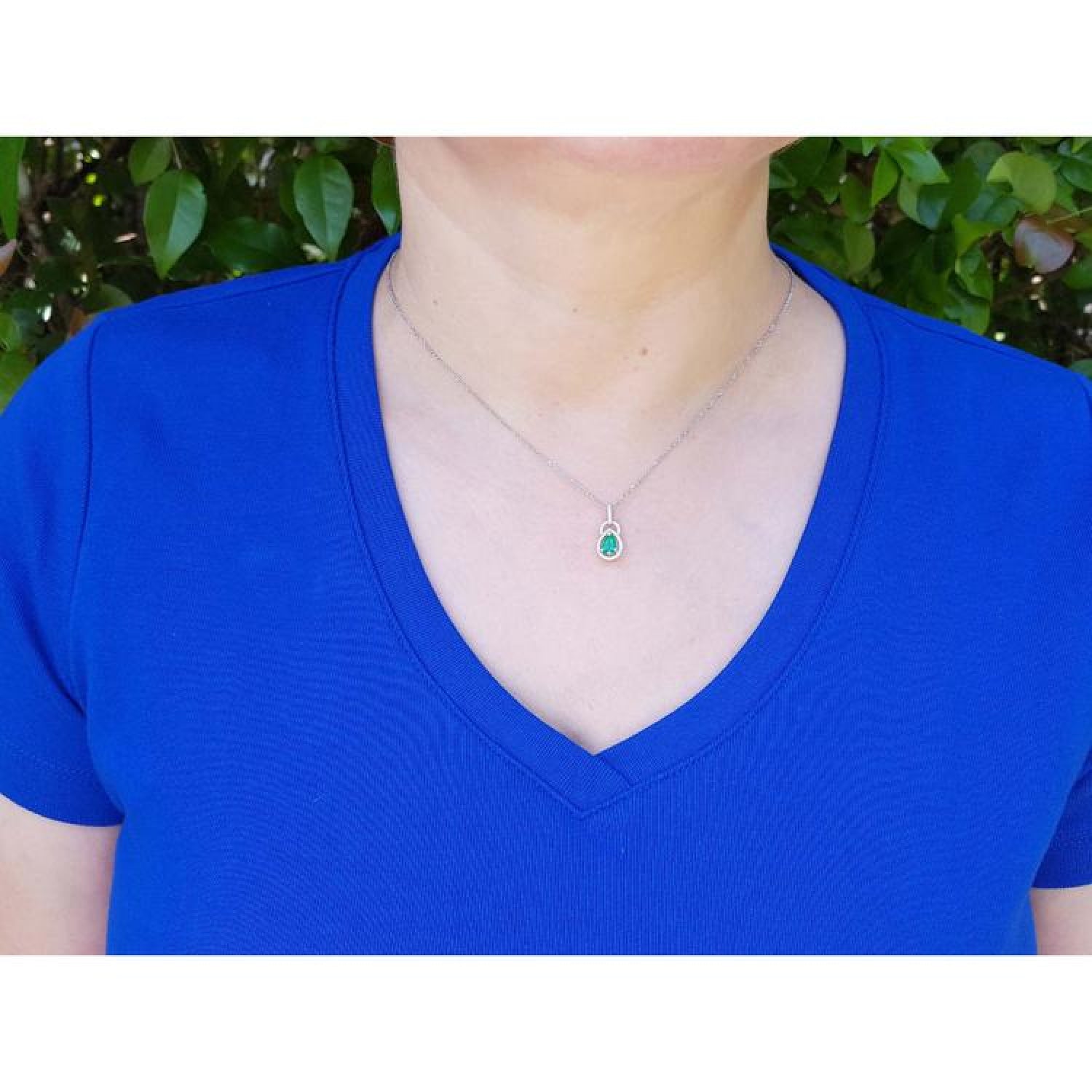 Pear-shaped Colombian emerald and diamond halo pendant on a 14K white gold chain, worn on a woman's neck.