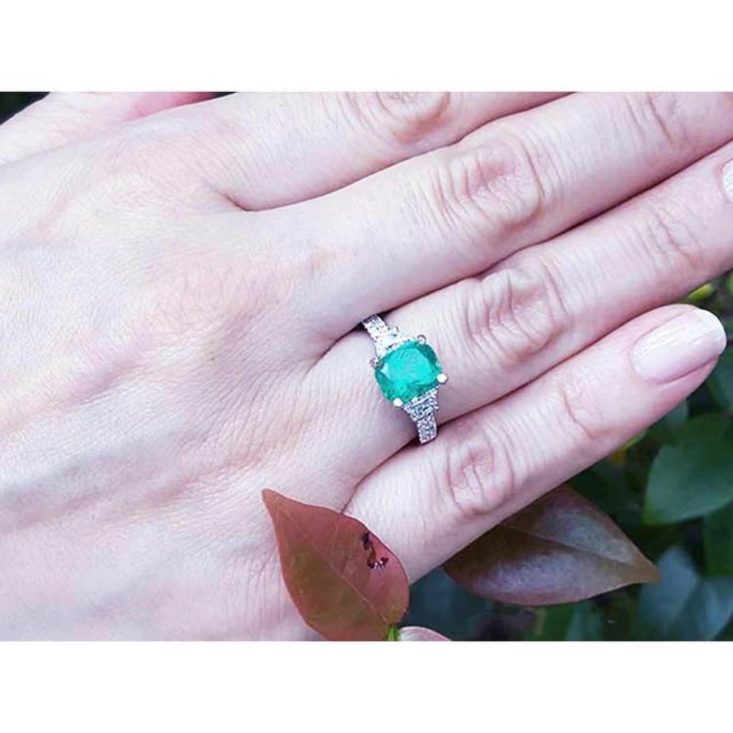 18K white gold ring with cushion cut emerald and trapezoid side diamonds on a hand.