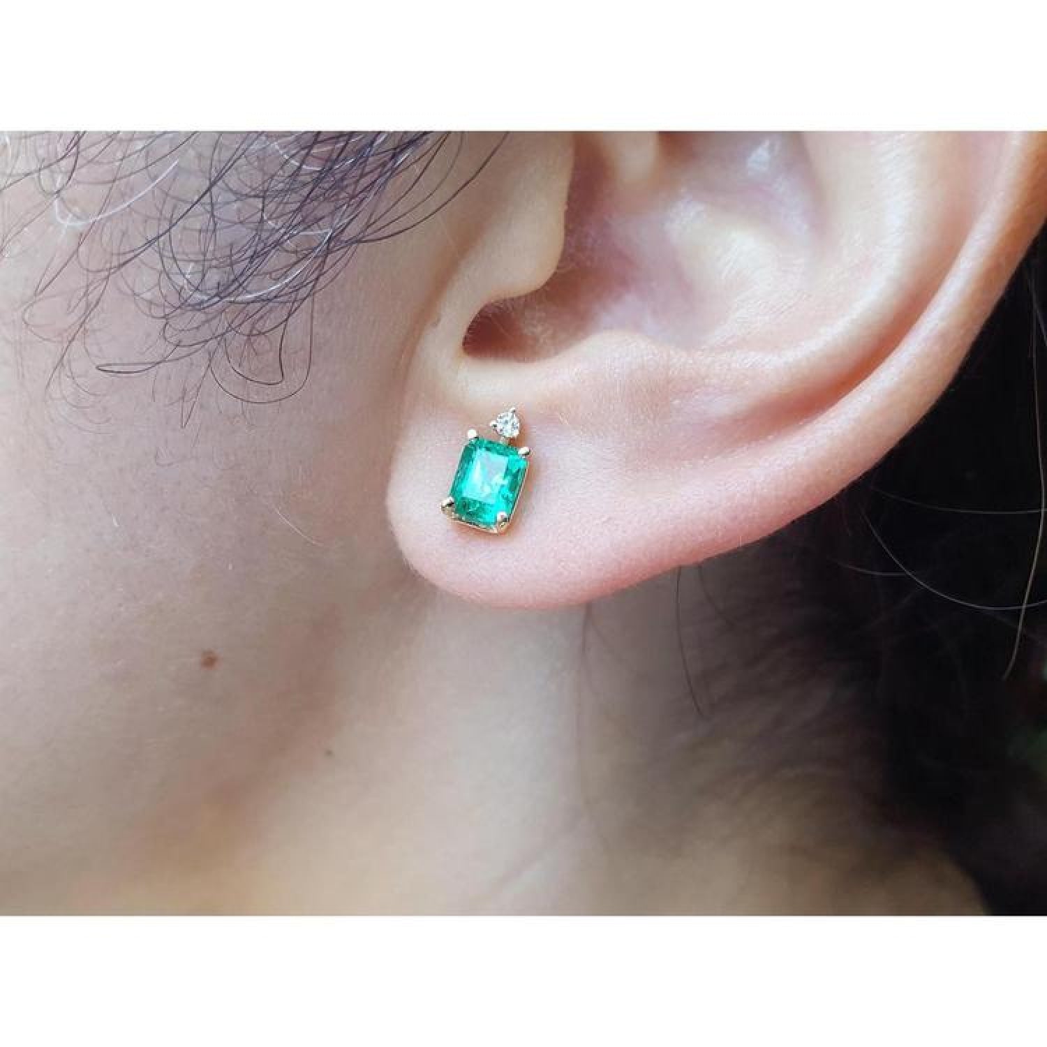 Rectangular Colombian emerald and diamond stud earring in 14K yellow gold on an ear.