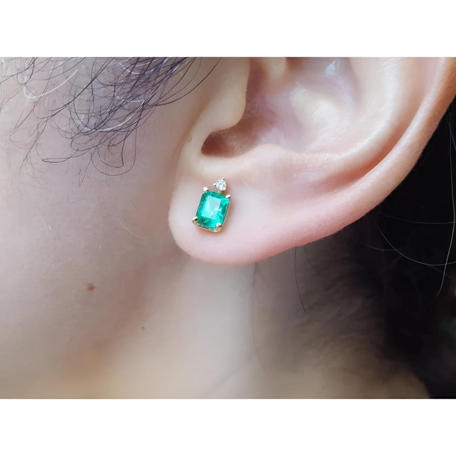 Rectangular Colombian emerald and diamond stud earring in 14K yellow gold on an ear.
