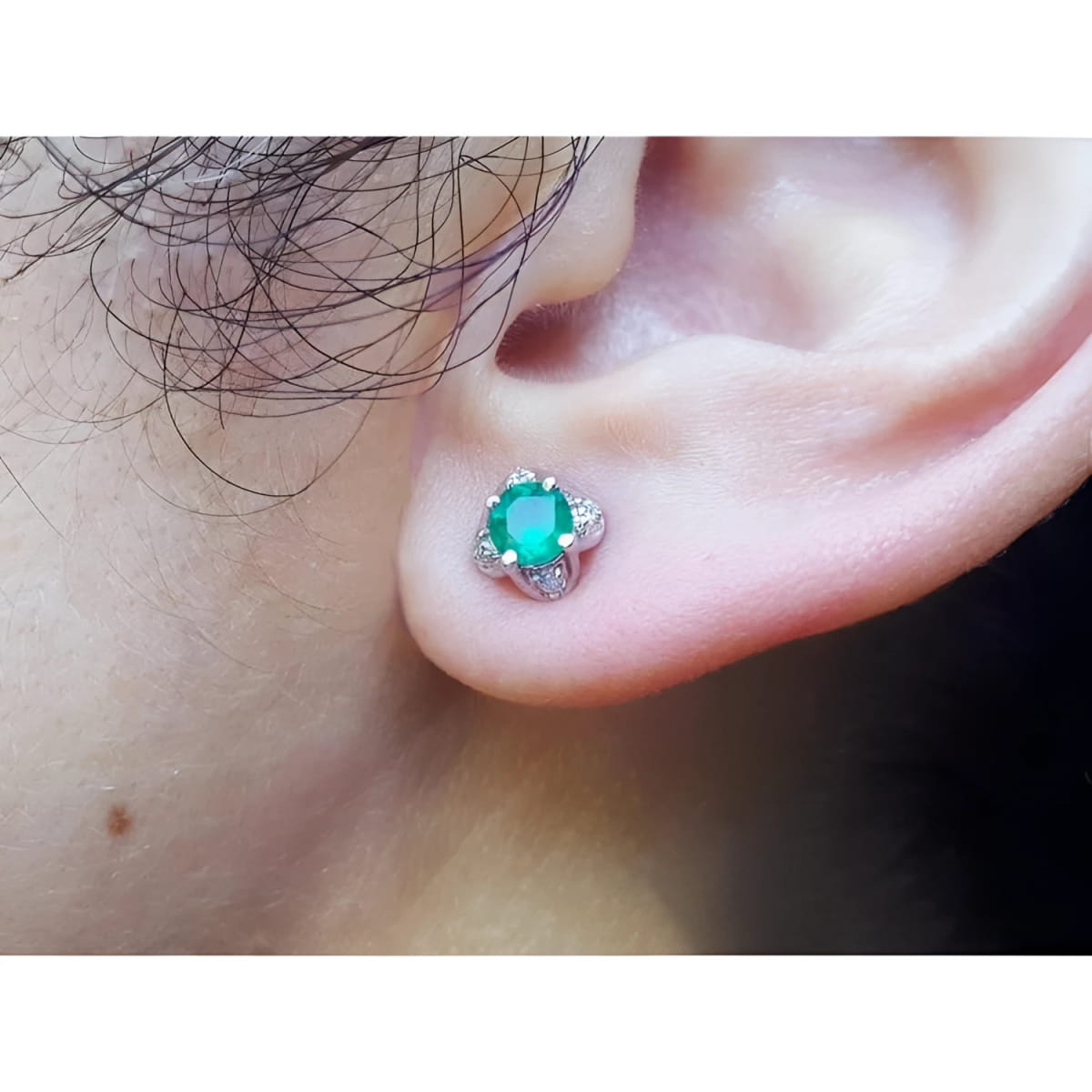 An ear wearing an emerald and diamond tulip stud earring in white gold.