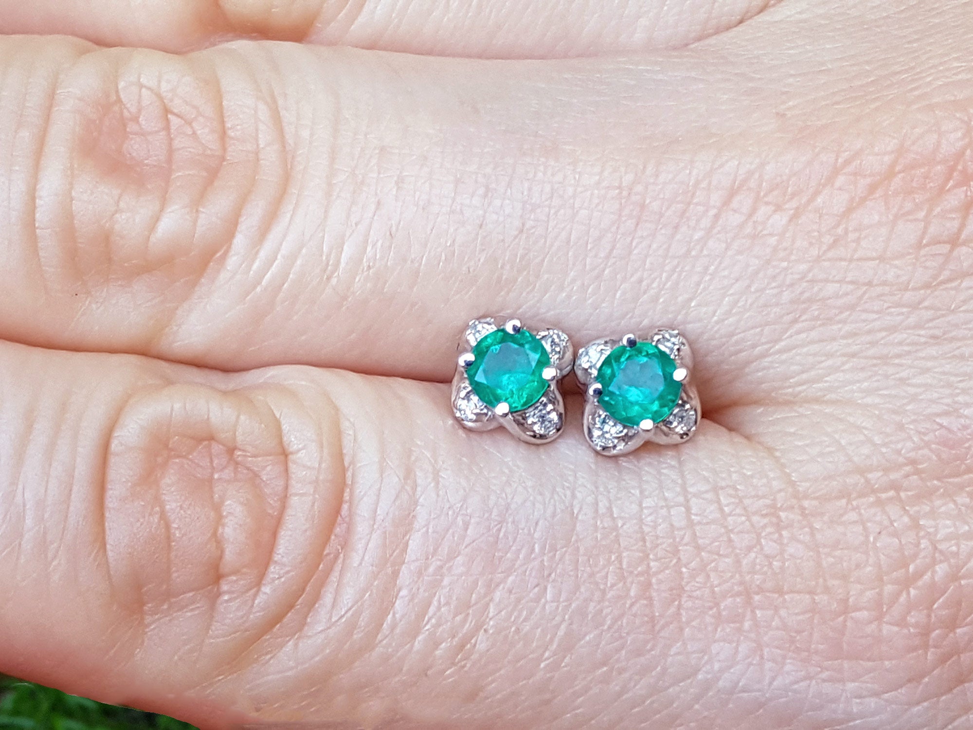 Emerald tulip stud earrings on a person&#39;s finger, top side view.