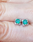 Emerald tulip stud earrings on a person's finger, top side view.