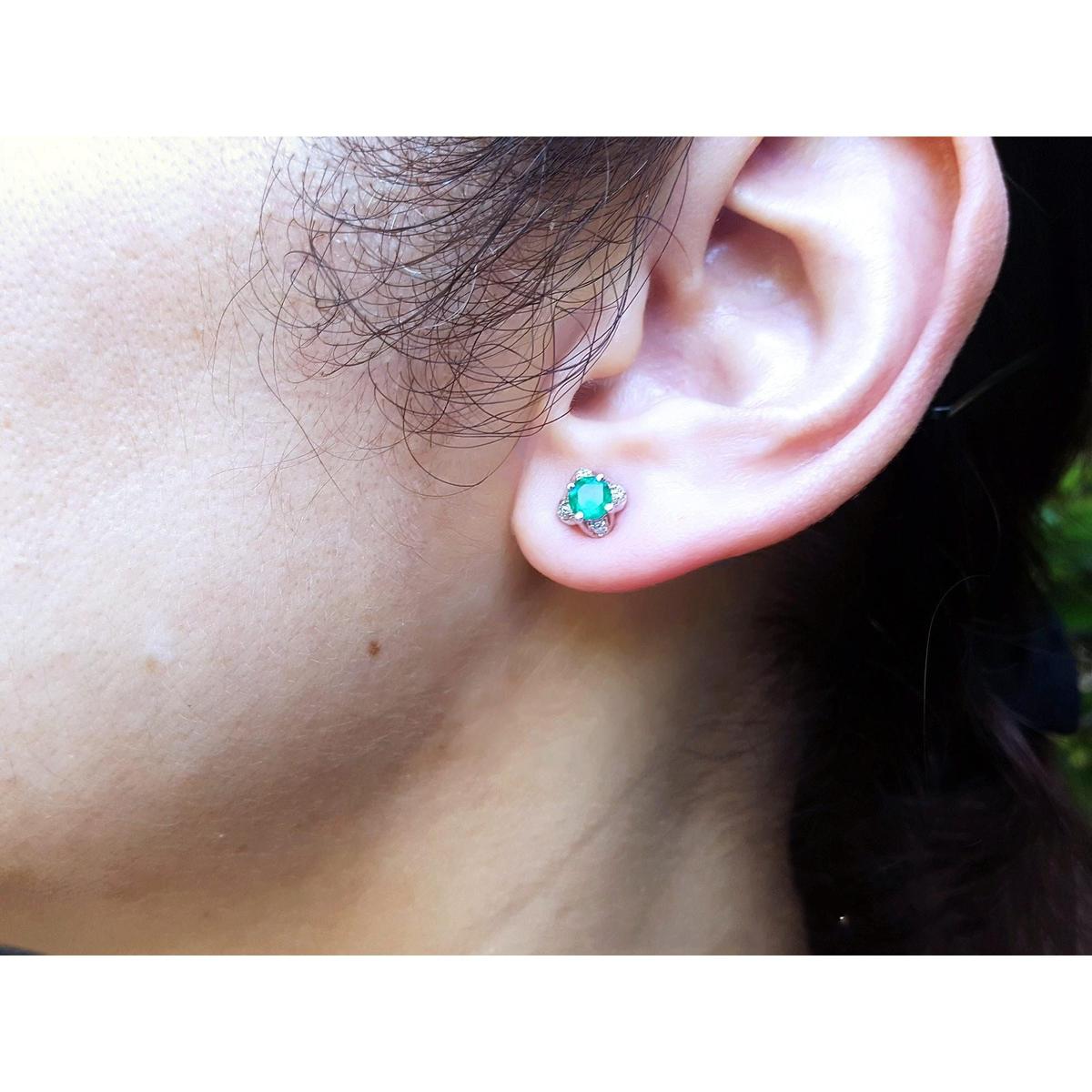 Close-up of a woman's ear wearing a tulip emerald and diamond stud earring with a blurred background