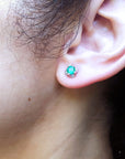 Close-up of a woman's ear wearing a tulip emerald and diamond stud earring with a blurred background