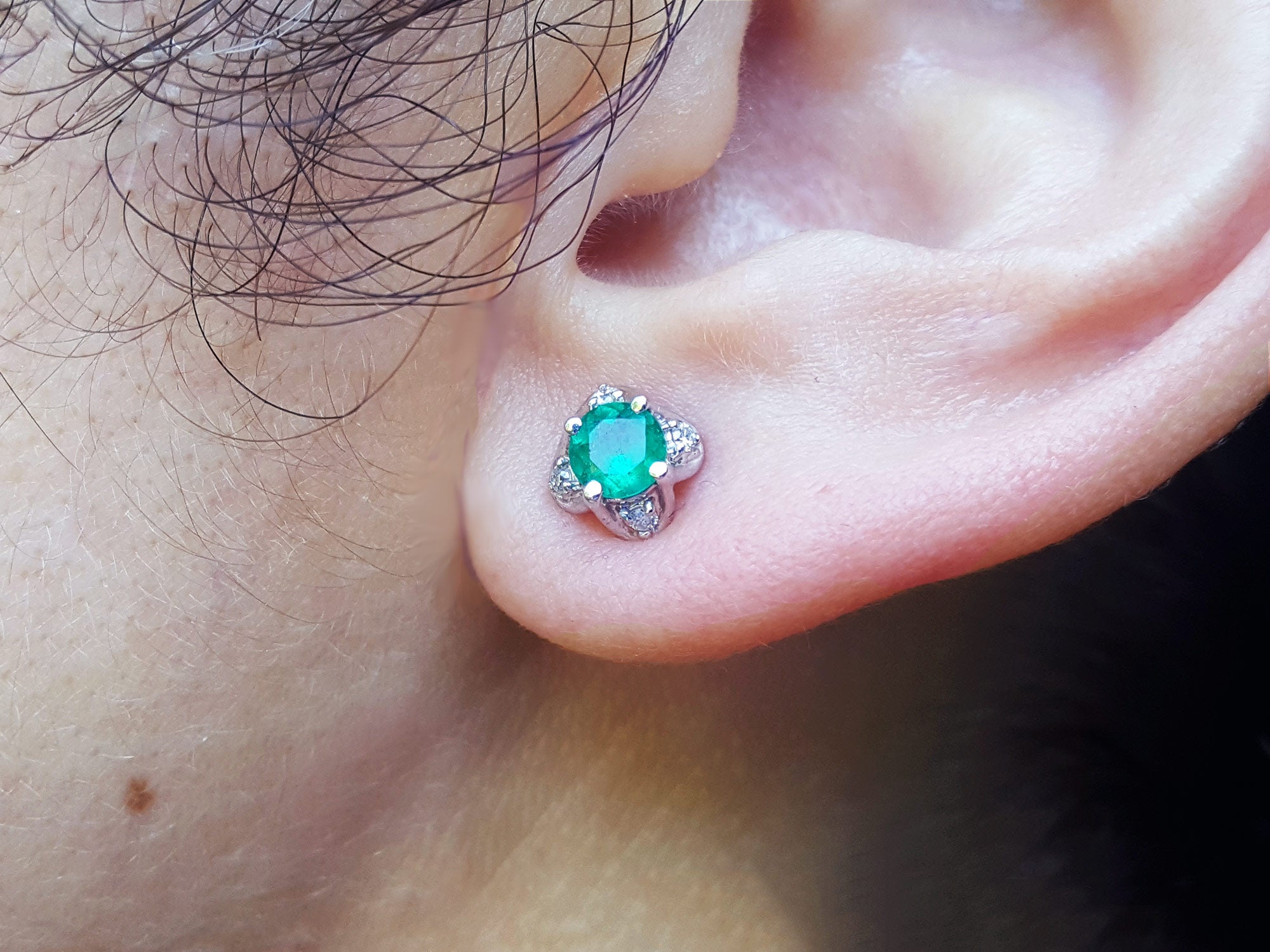 Close-up of an ear with a emerald and diamond tulip stud earring.