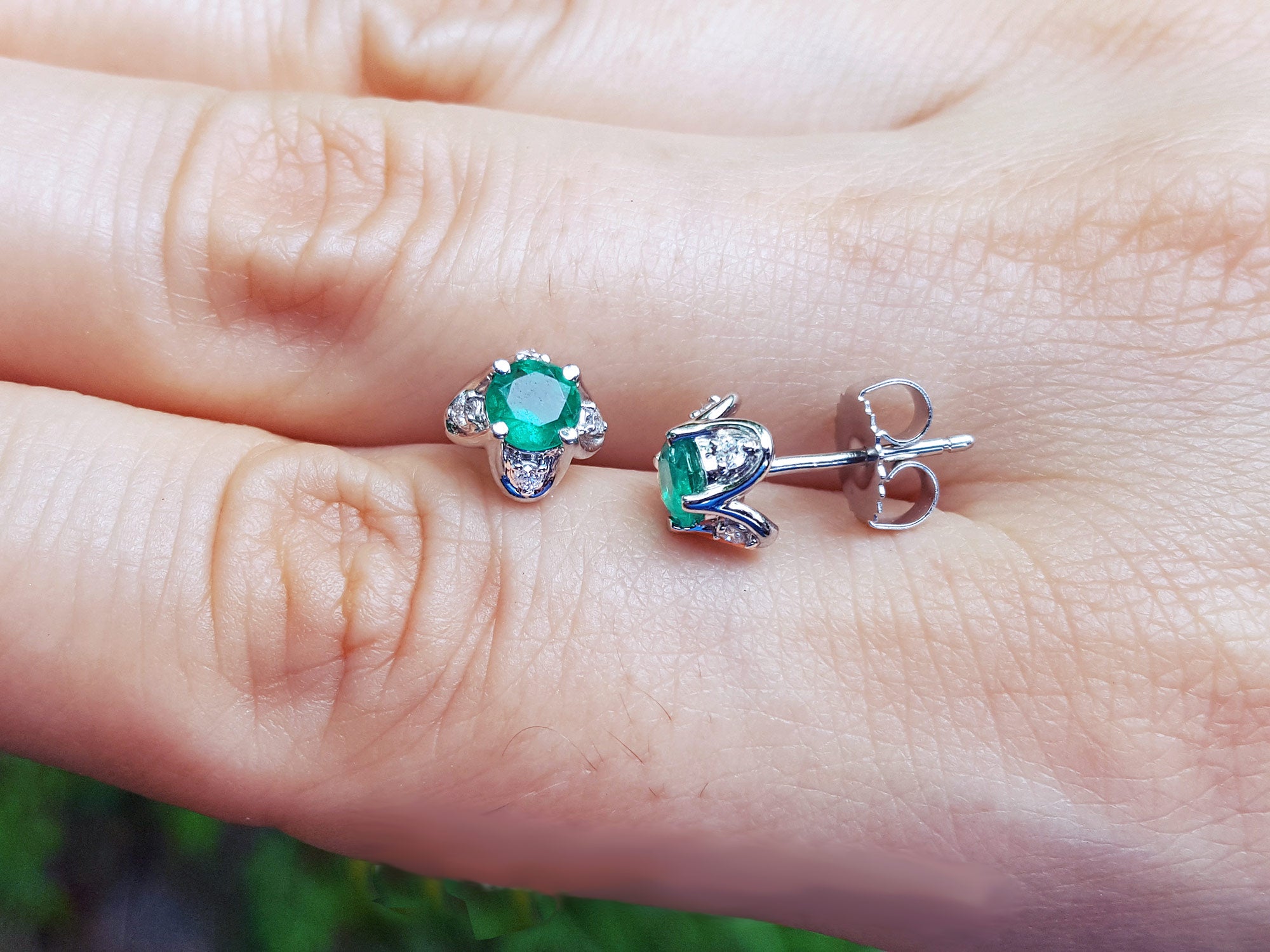 Women&#39;s gift emerald tulip stud earrings held between fingers on a light skin background.