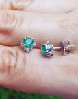 Women's gift emerald tulip stud earrings held between fingers on a light skin background.