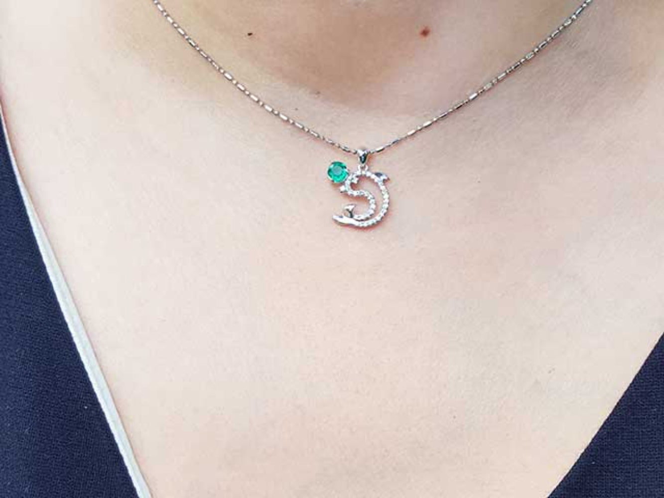 A round cut emerald dolphin pendant on a person&#39;s neck.