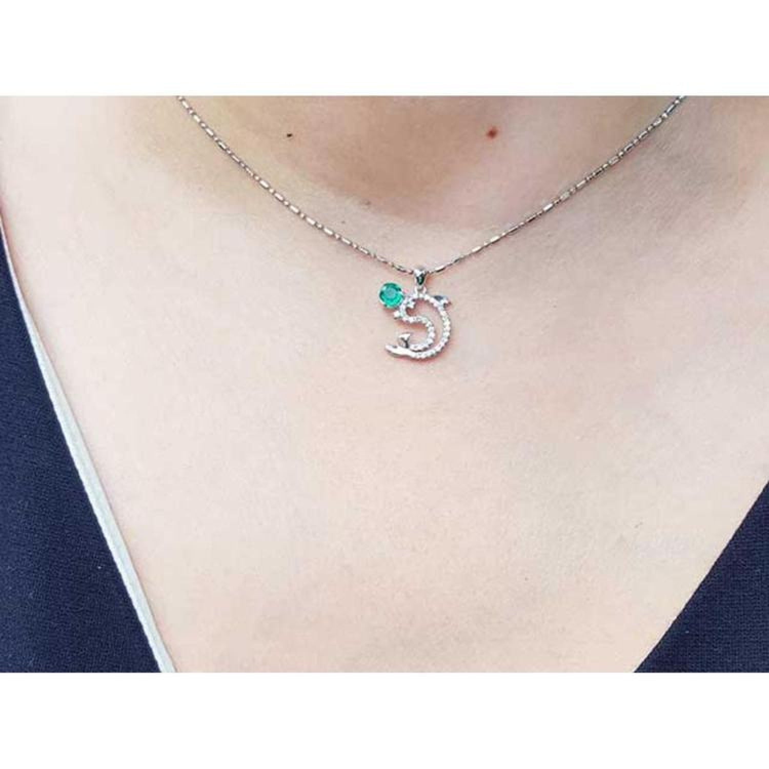 14K white gold dolphin pendant necklace with a deep green emerald and brilliant accents on a woman's neck.