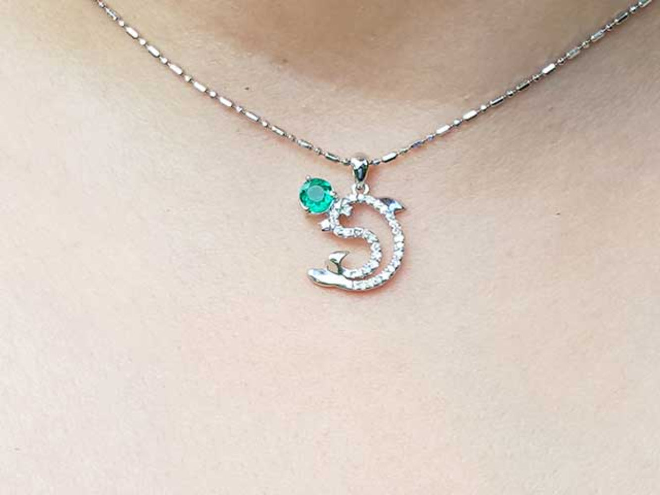 Necklace with a dolphin pendant with emerald and diamonds on a person's neck.