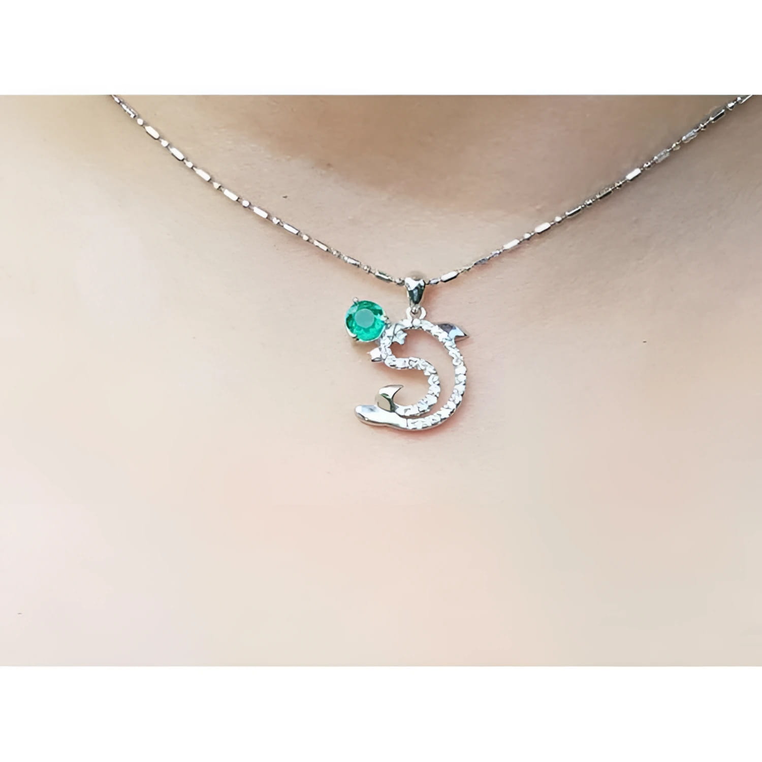 Necklace with a dolphin pendant with emerald and diamonds on a person's neck.