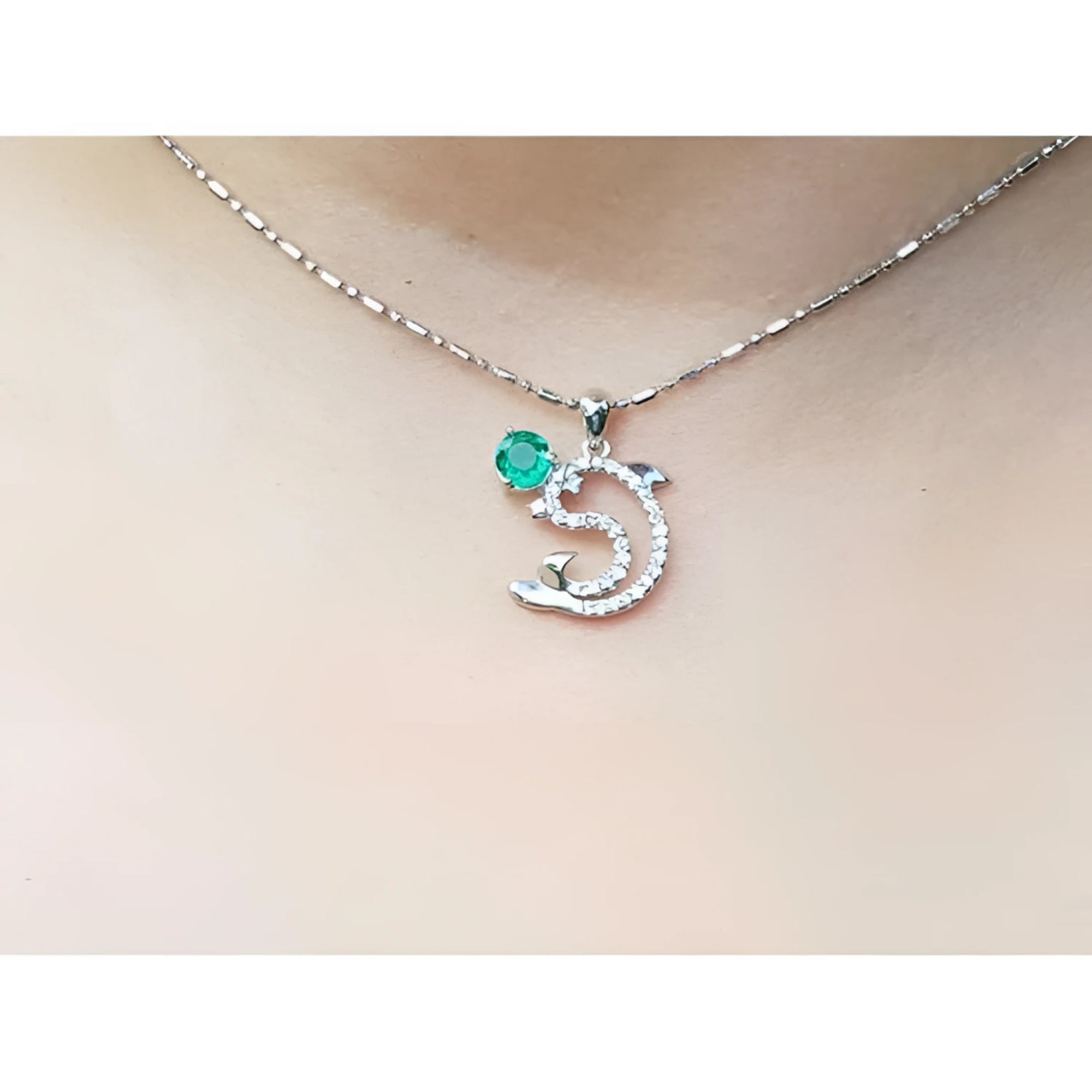 Necklace with a dolphin pendant with emerald and diamonds on a person's neck.