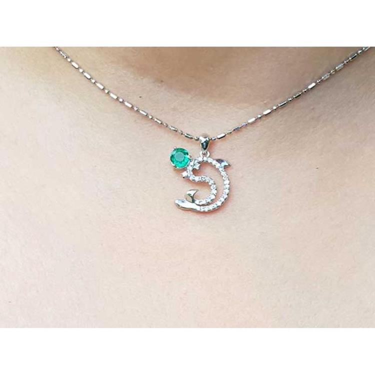 Necklace with a dolphin pendant with emerald and diamonds on a person's neck.