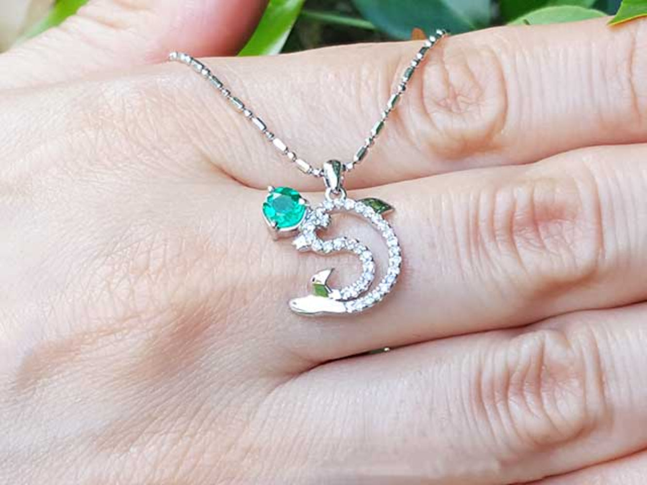 A 14K Solid white gold emerald dolphin pendant on a hand.